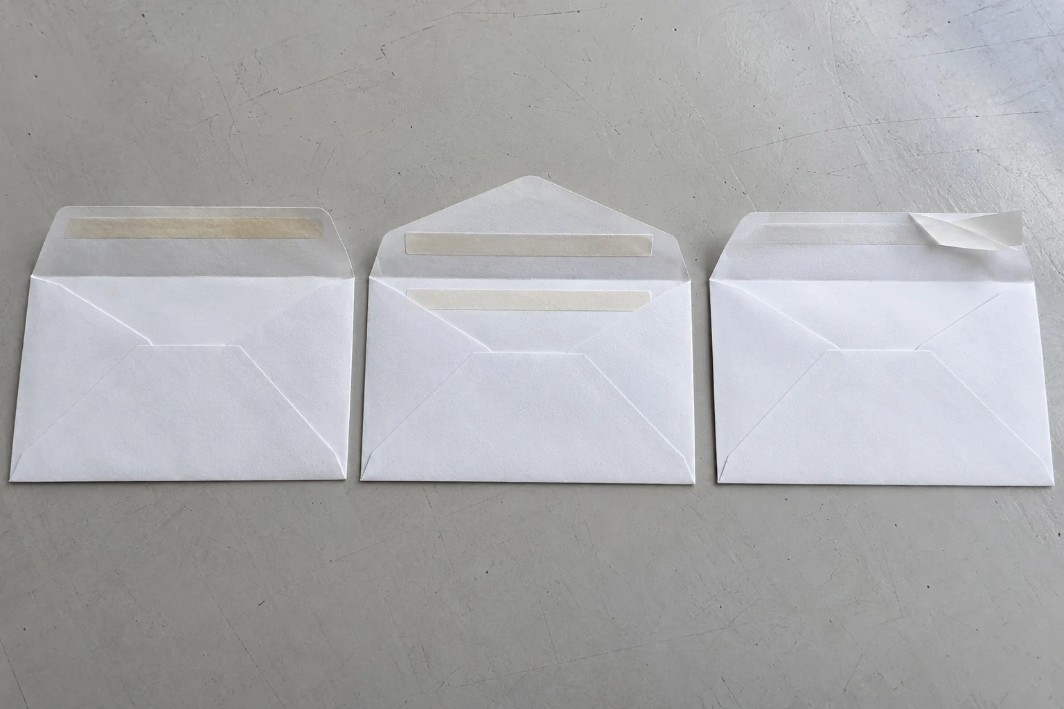 Three open white envelopes on a gray table, showing a single gum band, two matching cream bands and a partly lifted release strip.
