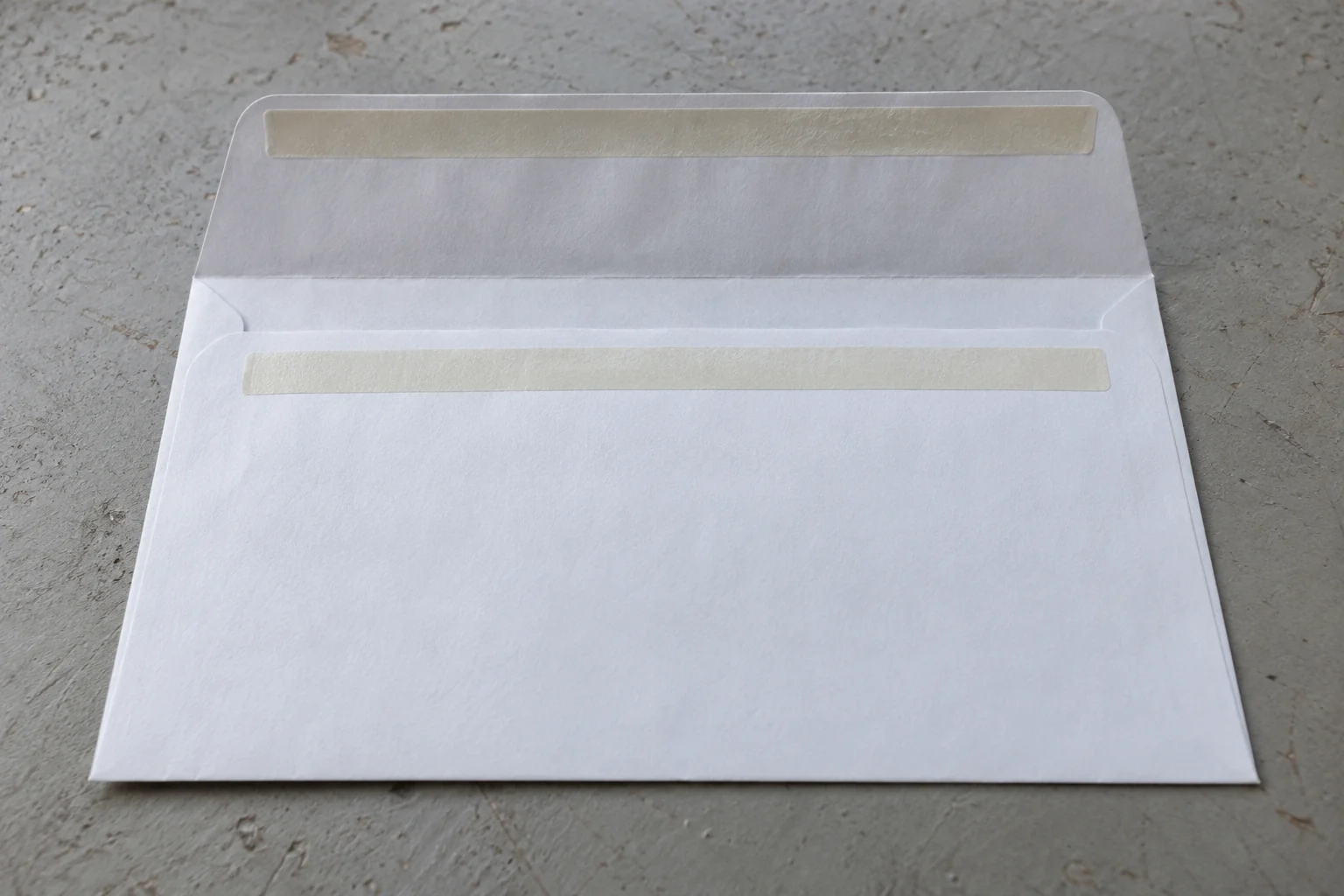 An open white envelope viewed from the back with one cream band on its raised flap and a matching band below the opening.